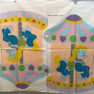 May include: A vintage fabric panel featuring two carousel horses with colorful details. The panel is divided into two sections, each with a carousel horse and a canopy. The canopies are decorated with hearts and stripes. The text "Rainbow Creations, Inc. 1983" is printed in the top right corner.