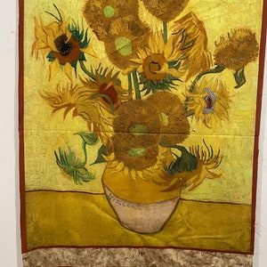 May include: A fabric wall hanging featuring a depiction of Van Gogh's "Sunflowers" painting. The artwork showcases a vase of sunflowers in shades of yellow, brown, and green, with a light yellow background and a decorative border.