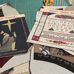 May include: Several jacquard-loomed tapestries with holiday and seasonal themes. One features the three wise men, a star, and a dark blue background. Another displays an alphabet, floral patterns, and the text "Bless Our Home."