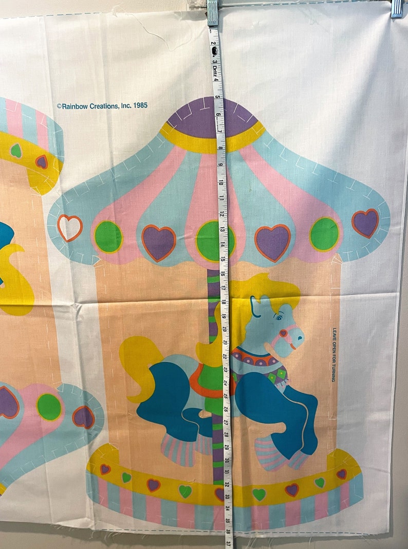 May include: A vintage fabric panel featuring a colorful carousel with a blue horse, pink, yellow, and green accents. The panel is marked "Rainbow Creations, Inc. 1985" and includes the text "Leave open for turning".
