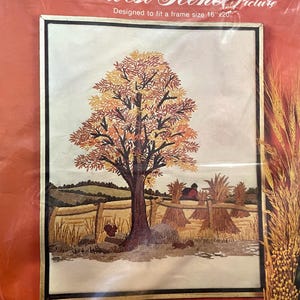 May include: A crewel embroidery kit featuring a fall harvest scene. The design includes a large tree with autumn-colored leaves, a fence, hay bales, and a red barn. The kit is designed to fit a 16" x 20" frame.