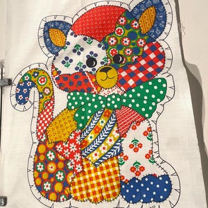 May include: A white fabric panel featuring a printed patchwork-style cat design with various colorful patterns including red, blue, yellow, and green floral, plaid, and polka dot motifs. A green polka dot bow is at the neck. Text reads LEAVE OPEN FOR STUFFING.