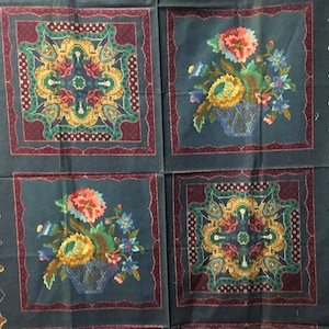 May include: A square fabric with a dark teal background features four decorative panels. Two panels display floral arrangements in baskets, while the other two showcase ornate, symmetrical designs. The borders are a deep burgundy with a paisley-like pattern.