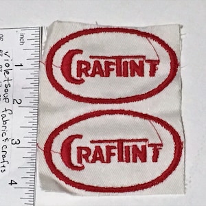May include: Two white fabric patches with red embroidered text and oval borders. Each patch features the word "CRAFTINT" in red. The patches are approximately 1 inch in height. Ideal for crafting and sewing projects.