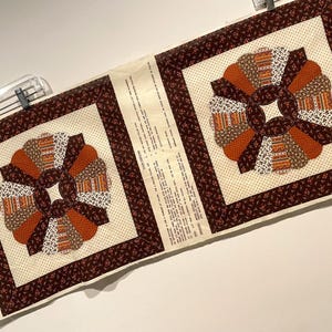 May include: A fabric panel for a trunk pillow featuring two square quilt blocks with circular fan patterns in shades of brown, orange, and cream. The fabric includes printed instructions and the text Trunk Pillow in the upper right corner.