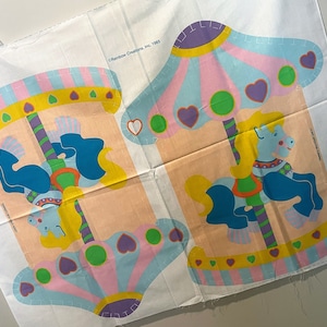 May include: A vintage fabric panel featuring a colorful carousel with two horses. The panel is printed with a light pink, blue, yellow, and green color scheme. The text "Rainbow Creations, Inc. 1985" is printed in the top right corner.