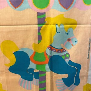 May include: A colorful fabric panel featuring a blue and yellow carousel horse with a striped pole and green, pink, and purple accents. The text "LEAVE OPEN FOR TURNING" is printed on the right side of the panel.