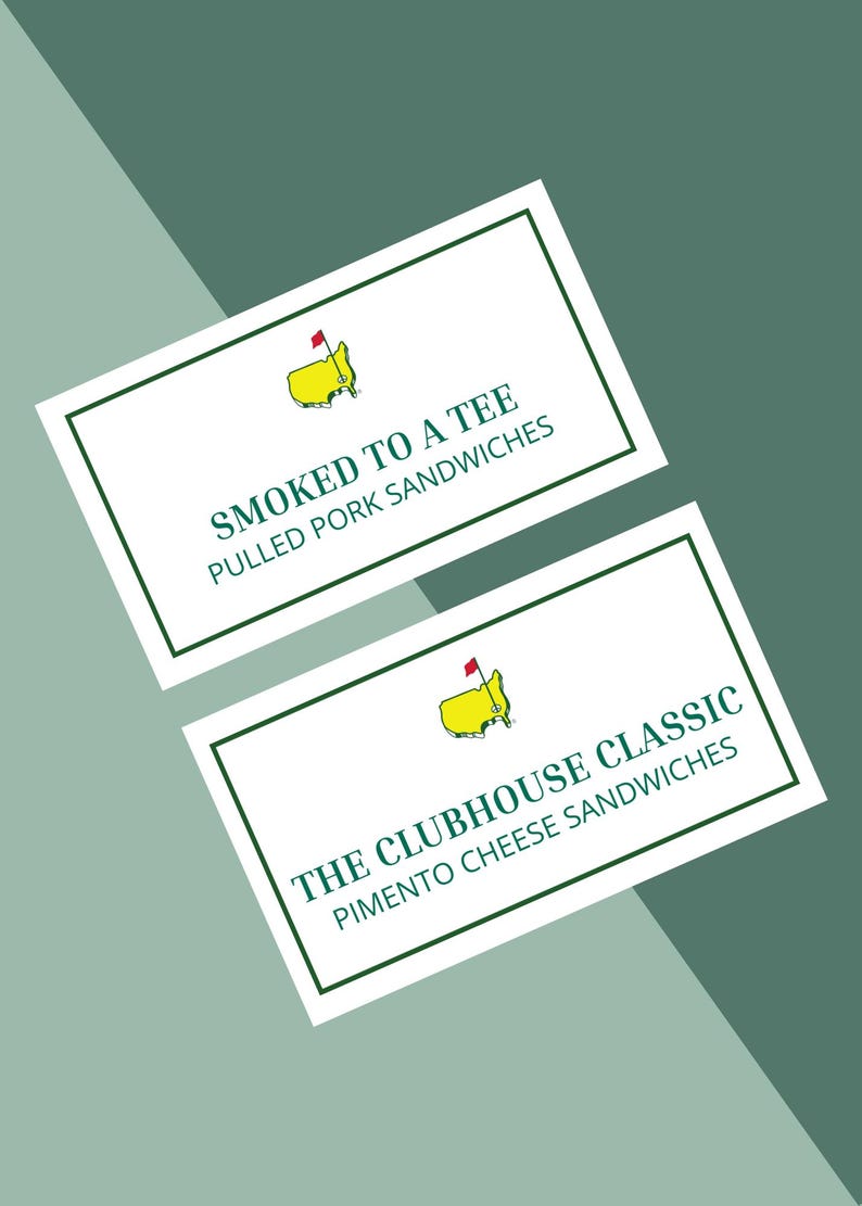 May include: Two white rectangular signs with green borders and text. The top sign reads "SMOKED TO A TEE" and "PULLED PORK SANDWICHES". The bottom sign reads "THE CLUBHOUSE CLASSIC" and "PIMENTO CHEESE SANDWICHES". Each sign has a yellow golf course logo.