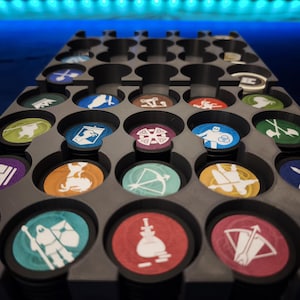 以下が含まれることがあります： カラフルなゲームトークンで満たされた灰色のプラスチック製ゲームトークンオーガナイザー。トークンは丸く、赤、青、緑など、さまざまなアイコンと色があります。オーガナイザーには、トークンを保持するための複数の円形スロットがあります。