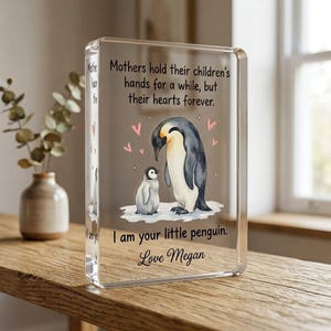 May include: A clear acrylic block with a penguin illustration. The image shows a parent penguin and a baby penguin with the text "Mothers hold their children's hands for a while, but their hearts forever." and "I am your little penguin. Love Megan."