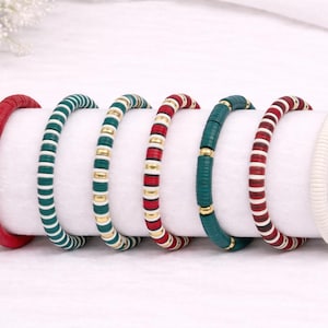 May include: A collection of colorful bracelets in various designs. The bracelets are in shades of red, green, white, and gold. The bracelets are made of small, flat beads strung together to form a circular shape. The bracelets are displayed on a white surface.