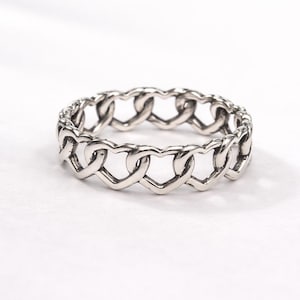 Könnte beinhalten: Ein silberner Ring mit einem durchgehenden herzförmigen Kettendesign. Der Ring besteht aus einem glänzenden, metallischen Material und liegt auf einer weißen Oberfläche. Die Herzen sind ineinander verschlungen und erzeugen ein kettenartiges Aussehen.