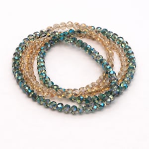 May include: Four beaded bracelets in shades of gold and teal. The bracelets are made of small, faceted beads, creating a sparkling effect. The bracelets are arranged in a circular pattern against a white background.