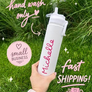 May include: A white water bottle with a straw lid and the name Michelle printed in pink script. The bottle features text that reads hand wash only, small business, and fast shipping. The design includes pink heart icons and a pink delivery truck graphic.