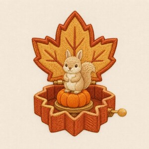 May include: An embroidered music box shaped like a maple leaf with a hinged lid. Inside, a small beige squirrel sits atop a round orange pumpkin. The embroidery features detailed stitching in shades of orange, brown, and tan, with a small metal crank.