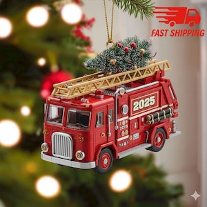 May include: A red Christmas ornament shaped like a vintage fire truck, complete with a ladder and a small Christmas tree on top. The ornament has the year "2025" displayed on the side. The background is blurred with Christmas lights.