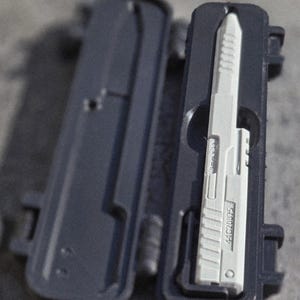 May include: A gray plastic case, open to reveal a white, rectangular object with a ridged surface. The object is labeled with the number "44C20975". The case is dark gray and has a hinged design.