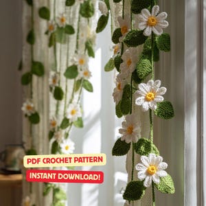 Può includere: Ghirlanda di margherite all'uncinetto con petali bianchi e centri gialli, accentuata da foglie verdi. La ghirlanda è appesa davanti a una finestra. Il testo sull'immagine recita "PDF Crochet Pattern" e "Instant Download!"