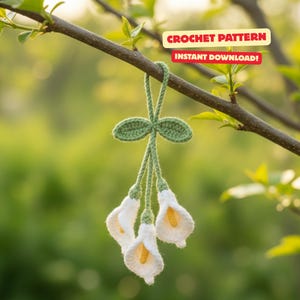 Könnte beinhalten: Gehäkelter Calla-Lilien-Schmuck mit weißen Blütenblättern und gelben Zentren, aufgehängt an einem grünen Stiel und Blättern. Der Schmuck hängt an einem Ast. Der Text auf dem Bild lautet "CROCHET PATTERN" und "INSTANT DOWNLOAD!"