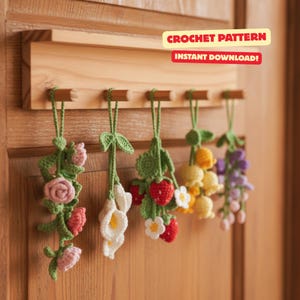 Op de afbeelding: Een houten wanddisplay met vijf gehaakte bloemornamenten. De ornamenten omvatten rozen, calla lelies, aardbeien, gele bloemen en paarse blauwe regen. De tekst "CROCHET PATTERN" en "INSTANT DOWNLOAD!" wordt weergegeven op het houten bord.