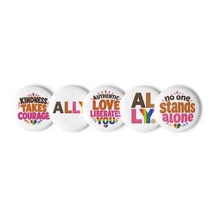 May include: Five circular white pinback buttons featuring colorful text and graphics. The buttons display the phrases: KINDNESS TAKES COURAGE, ALLY, AUTHENTIC LOVE LIBERATES YOU, ALLY, and no one stands alone, accented with rainbow-colored heart icons.