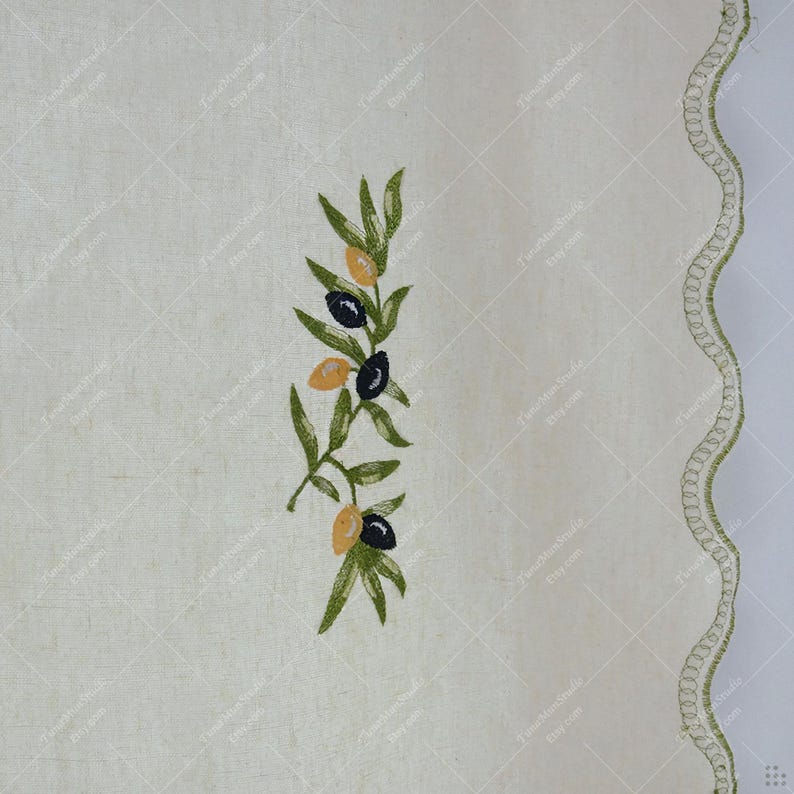 May include: Cream-colored fabric with an embroidered olive branch design. The branch features green leaves and black and yellow olives. A scalloped edge with green stitching borders the right side.