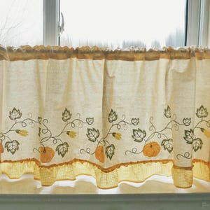 May include: Cream-coloured kitchen curtain with a pumpkin and leaf design. The curtain features embroidered pumpkins, leaves, and vines in orange, green, and yellow. A yellow and white checked trim adds a decorative touch.