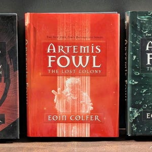 May include: Three hardcover books from the "Artemis Fowl" series by Eoin Colfer. The books are titled "The Opal Deception", "The Lost Colony", and "The Time Paradox". Each book has a unique cover design with the series title prominently displayed.
