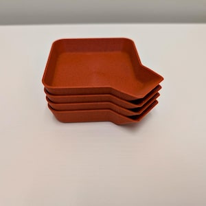 May include: A stack of four terracotta-colored, rectangular trays with a unique angled design. The trays have a speckled texture and are stacked neatly on a white surface. The trays are likely for serving or display.