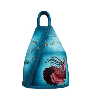 Peut inclure: Sac à dos en cuir bleu sarcelle avec une poignée supérieure et une bandoulière réglable. L'avant présente une illustration colorée d'une personne tenant un cerf-volant. Le cerf-volant est relié à une guirlande de décorations en forme d'étoiles.