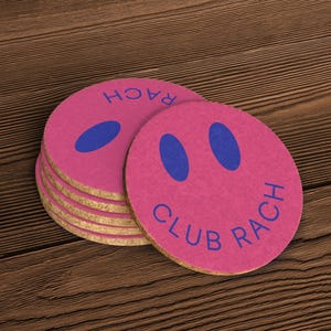 A close up of a stack of coasters on a wooden surface. The coasters are pink with blue detailing.