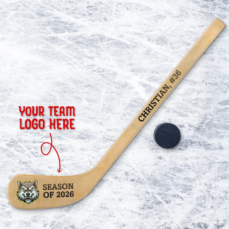 Personalized mini wooden hockey stick featuring custom team logo printed on the blade with space for team name and season text, shown on an ice background with a hockey puck.