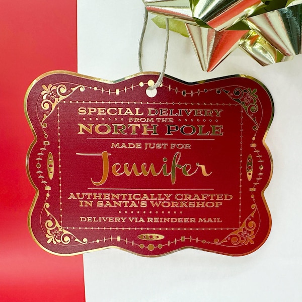 Puede incluir: Una etiqueta de regalo roja y dorada con el texto "SPECIAL DELIVERY FROM THE NORTH POLE MADE JUST FOR Jennifer AUTHENTICALLY CRAFTED IN SANTA'S WORKSHOP DELIVERY VIA REINDEER MAIL".