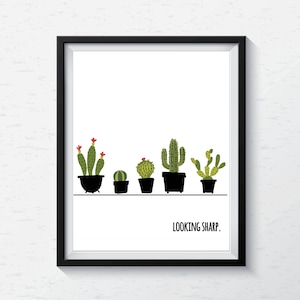 May include: A black framed print with a white background featuring a line of five potted cacti with the text "LOOKING SHARP." below.