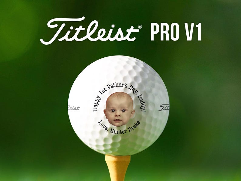 Top text reads Titleist Pro V1. Titleist golf ball is shown on a golf tee against a dark green background. Ball is shown with 1st Fathers Day photo design in black text color option.