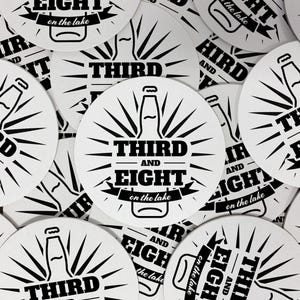 Multiple coasters spread in all different directions. Coasters display a custom design showing a black and white logo for a bar.