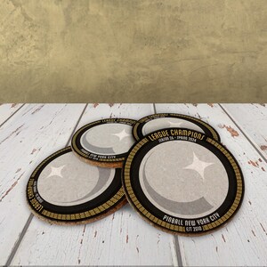 A stack of coasters sit on a wooden surface. They are black with yellow and grey detailing, and white and yellow text.