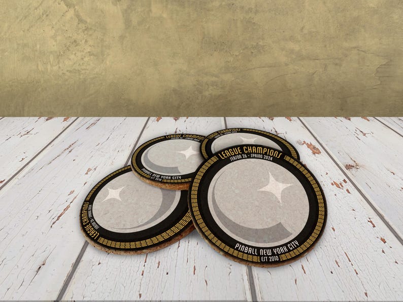 A stack of coasters sit on a wooden surface. They are black with yellow and grey detailing, and white and yellow text.