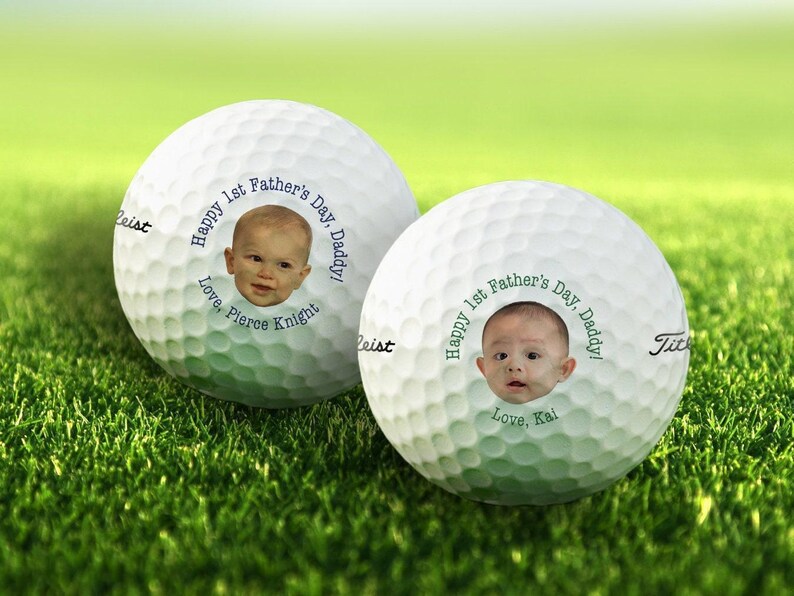 Titleist golf balls are shown on patch of grass. Both golf balls show 1st Fathers Day photo design in blue and green text color options.