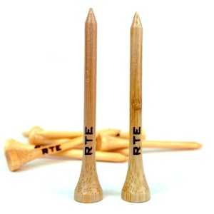 May include: Two wooden golf tees with the word "RTE" engraved on them. The tees are brown and have a pointed top. There are other golf tees in the background.