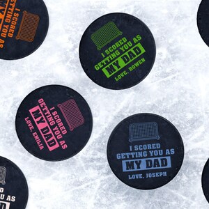 Multiple hockey pucks ontop of ice rink with I scored you as my dad designs printed ontop with different names and colors