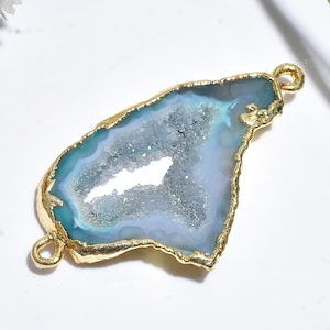 May include: A blue and white geode pendant with a gold-coloured trim. The pendant has a unique, irregular shape and two small loops for attaching to a chain or other jewellery component. The geode's interior has a crystalline texture.