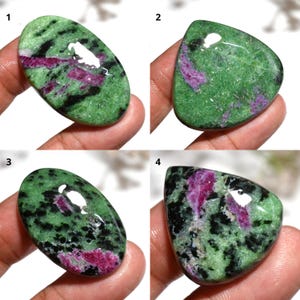 Puede incluir: Cuatro piedras preciosas pulidas de rubí zoisita. Las piedras muestran una mezcla de colores verde, negro y magenta. Cada piedra tiene una forma única, con formas ovaladas y triangulares. Las piedras preciosas se sostienen en una mano.
