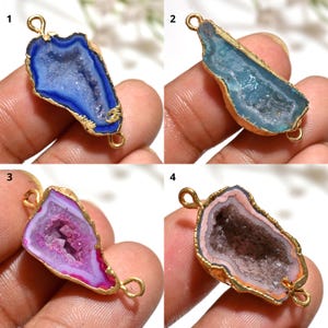 May include: Four gemstone pendants with gold-coloured metal edging. The gemstones are in shades of blue, teal, pink, and peach. Each pendant has a loop at the top and bottom for attaching to a chain or other jewellery component.
