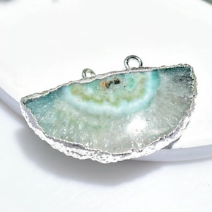 May include: A semi-circular pendant featuring a polished, light blue and green agate stone with a silver-coloured metal trim. The stone has a natural, layered pattern and two small loops for attaching to a chain or cord.