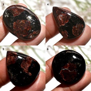 May include: Four polished gemstones with a mix of black and reddish-brown colors. The stones have various shapes, including oval, teardrop, and round. The gemstones are smooth and reflective, with a natural, earthy appearance.