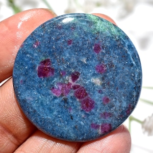 May include: A circular polished gemstone featuring a deep blue base colour with scattered, vibrant magenta-red inclusions and small flecks of dark mineral deposits throughout the surface, creating a natural, mottled, and textured appearance.