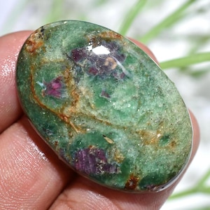 May include: Oval-shaped gemstone with a green base color and inclusions of deep red and brown. The polished surface reflects light, highlighting the natural patterns and textures of the stone. This gemstone is ideal for jewelry making.