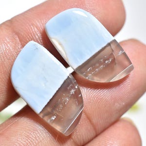 May include: Two polished gemstones, each with a light blue upper section and a clear, light brown lower section. The stones are rectangular with rounded edges. The gemstones are semi-transparent.