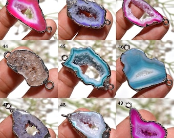 May include: A collection of nine gemstone pendants in various colors, including pink, purple, blue, and brown. Each pendant has a unique, irregular shape with a hollow center and a silver-colored metal frame. The pendants are displayed against a neutral background.
